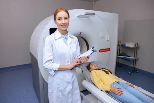 小女孩躺在Mri扫描仪的桌子上 而女性放射技师则开始进行现代健康诊断 — 图库照片