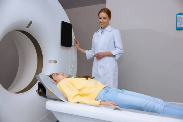 小女孩躺在Mri扫描仪的桌子上 而女性放射技师按下控制面板上的按钮 现代健康诊断 — 图库照片