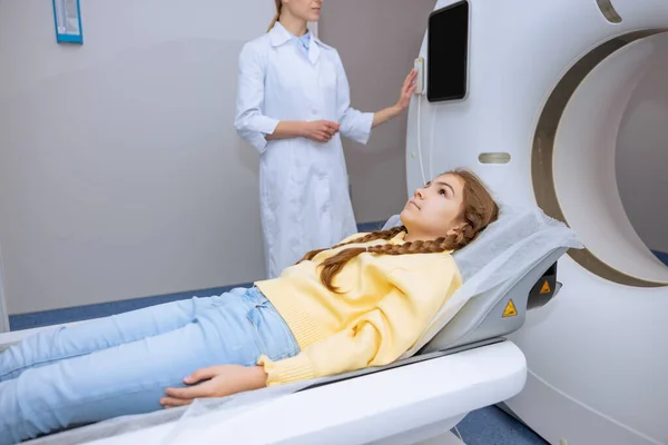 小女孩躺在Mri扫描仪的桌子上 而女性放射技师按下控制面板上的按钮 现代健康诊断 — 图库照片
