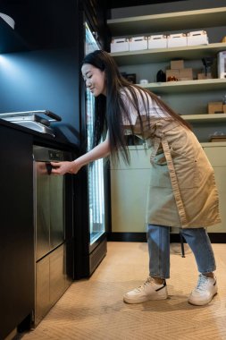 Gülümseyen, mutlu, genç bir kafe çalışanının bulaşık makinesinin kapısını kapatması.