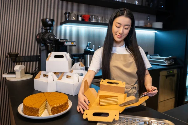 Coffeehouse employee placing a piece of dessert into the cardboard box using a cake server