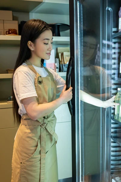Gülümseyen Genç Uzun Saçlı Asyalı Kadın Buzdolabındaki Şişeye Uzanıyor — Stok fotoğraf