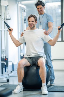 Fizik tedavi. Genç adam rehabilitasyon merkezinde eğitmenle fizik tedavi görüyor.