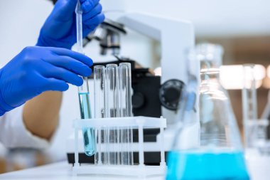 Kimya laboratuvarında çalışan tanınmayan bir araştırmacı, mavi eldivenli bir doktor moleküler biyoloji araştırması için pipet ve tüp kullanıyor..