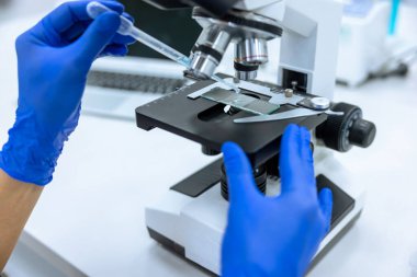 Tanımlanamayan araştırmacılar yeni ilaç örneklerini incelemek ya da geliştirmek için laboratuarda pipet ve mikroskop kullanıyor..