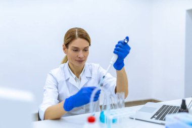 Koruyucu eldivenli çekici kadın bilim adamı bilimsel kimya laboratuarındaki bir pipetle test tüpüne sıvı madde atıyor..