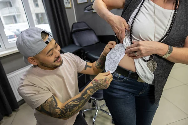在纹身沙龙里与纹身大师一起选择纹身的成年女性 — 图库照片