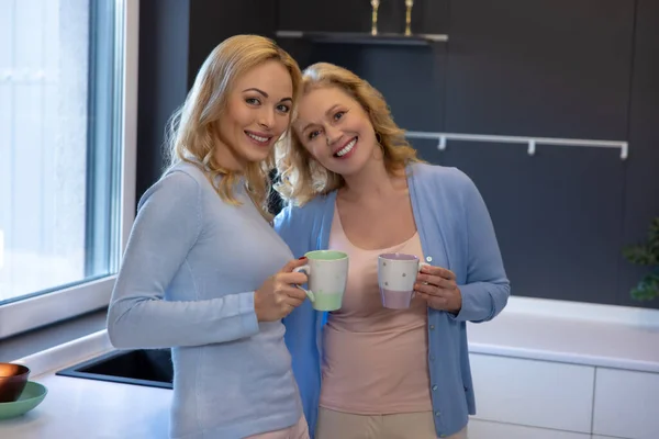 Dvě Usmívající Krásné Ženy Keramickými Hrnky Rukou Stojí Spolu Kuchyni — Stock fotografie
