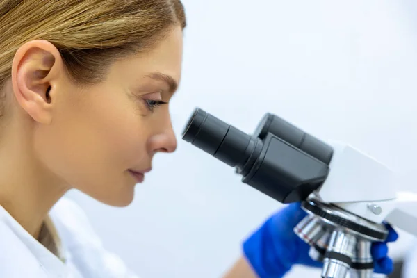 Mulher Loira Assistente Laboratório Luvas Azuis Olha Microscópio Fórmula Química — Fotografia de Stock