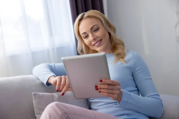 Mujer Sonriente Sentada Cómodo Sofá Mirando Tableta Digital Sus Manos — Foto de Stock