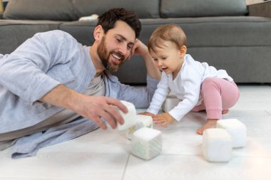 Sakallı baba, yeni yürümeye başlayan çocukla evde küplerle yerde oynuyor..