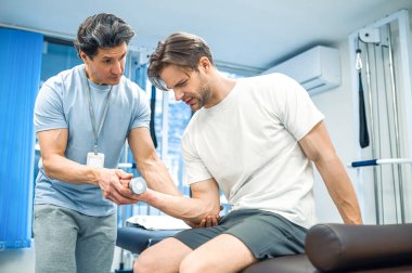 Rehabilitasyon. Kanepede oturan ve kolunu çalıştıran bir erkek hasta.