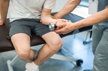 Rehabilitasyon. Kanepede oturan ve kolunu çalıştıran bir erkek hasta.