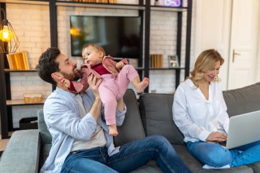 Baba, yeni yürümeye başlayan kızıyla oynuyor. Kadın serbest çalışıyor. Aile üzerinde çalışıyor..