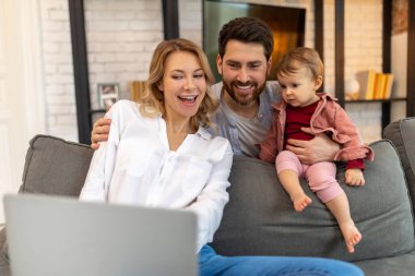 Baba, bebek kızıyla oynarken dizüstü bilgisayara bakıyor. Kanepede oturup, video bağlantısı kuruyor..