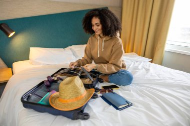 Tatile hazırım. Genç kıvırcık saçlı kadın tatile hazırlanıyor ve mutlu görünüyor.