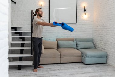 Atletik adam evde egzersiz yapmaya hazırlanırken yoga minderini açıyor..