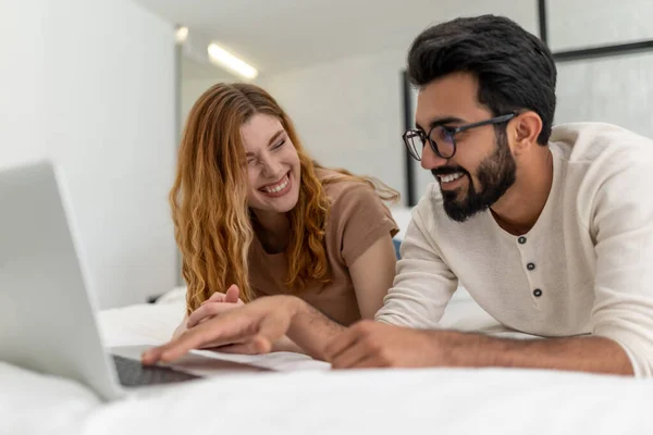 若い幸せなカップルは一緒に愛と笑みを浮かべてベッドサーフィンインターネット上に敷設ラップトップコンピュータを使用して自宅で余暇時間をお楽しみください — ストック写真