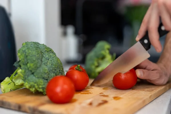 无法辨认的男性手在厨房里用锋利的刀把西红柿和西兰花切在切菜板上 做成沙拉 — 图库照片