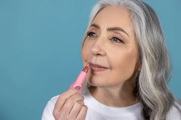 Makeup. Beautiful aging woman with lipstick doing makeup