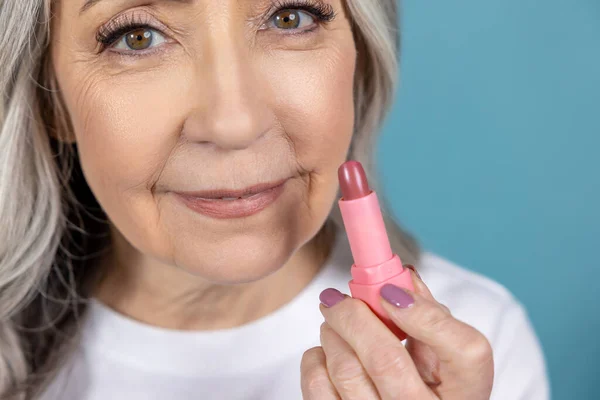 Makeup. Beautiful aging woman with lipstick doing makeup
