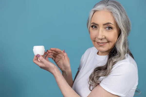 Gesichtspflege Langhaarige Seniorin Mit Gutem Aussehen Hält Ein Glas Gesichtscreme — Stockfoto