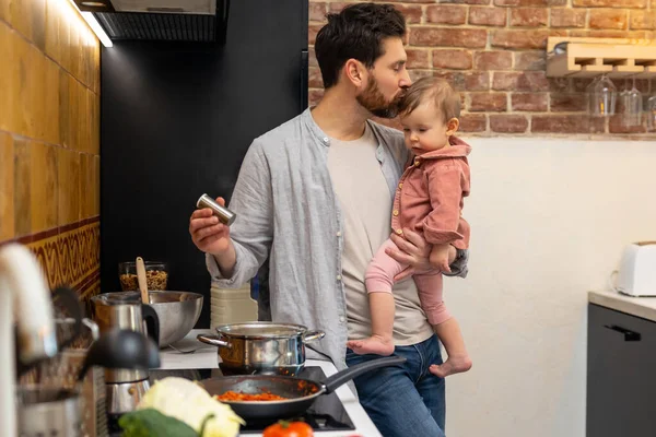 ひげを生やした男調理ディナーともに赤ちゃん娘で手立ってキッチン お父さん接吻幼児赤ちゃん — ストック写真