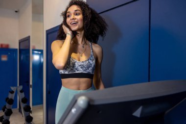 Koşu bandında. Koşu bandındaki kıvırcık saçlı genç kadın halinden memnun görünüyor.