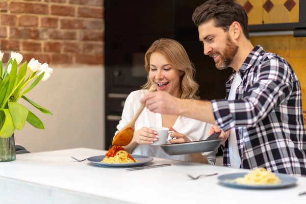 年轻夫妇在厨房里吃早餐 男人在做饭 女人在家里的厨房里坐在桌旁 — 图库照片