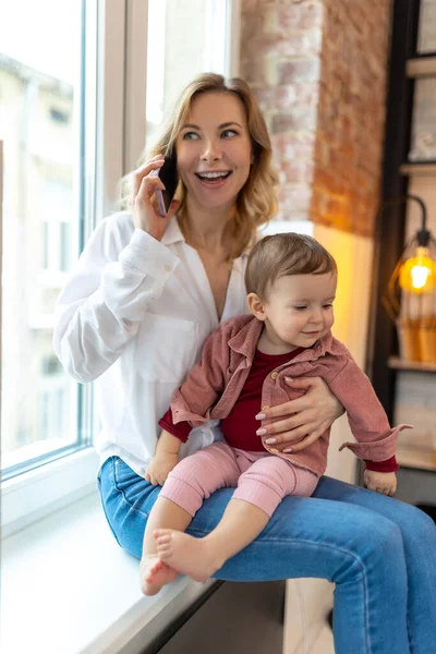 Fröhlich Lächelnde Frau Sitzt Auf Fensterbank Wohnzimmer Mit Handy Baby — Stockfoto
