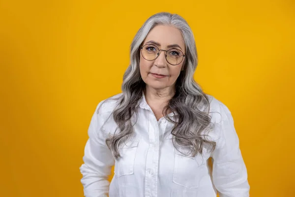 Woman in eyeglasses. Intelligent senior woman in eyeglasses on yellow background