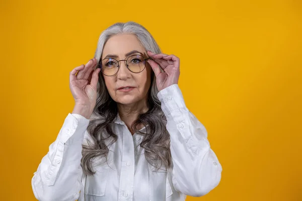 Woman in eyeglasses. Intelligent senior woman in eyeglasses on yellow background