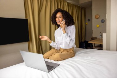 Otelde. Kıvırcık saçlı iş kadını otel odasında telefonda konuşuyor.