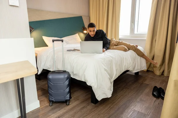 Готельному Номері Молодий Темноволосий Чоловік Лежить Ліжку Притулку Серфінгу Інтернет — стокове фото
