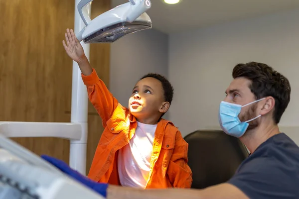 歯医者だ 歯科用ランプに興味を持っている暗い肌の男の子 — ストック写真
