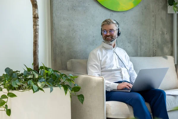Zadowolony Biznesmen Słuchawkach Siedzący Kanapie Piszący Laptopie Odwracając Wzrok — Zdjęcie stockowe