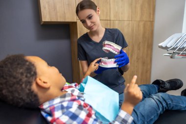 Diş hekimliğinde. Esmer tenli çocuk çene maketi ile ilgileniyor