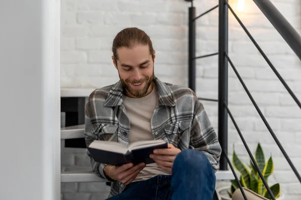 Joyful Jovem Homem Lendo Livro Enquanto Sentado Escadas Seu Apartamento — Fotografia de Stock