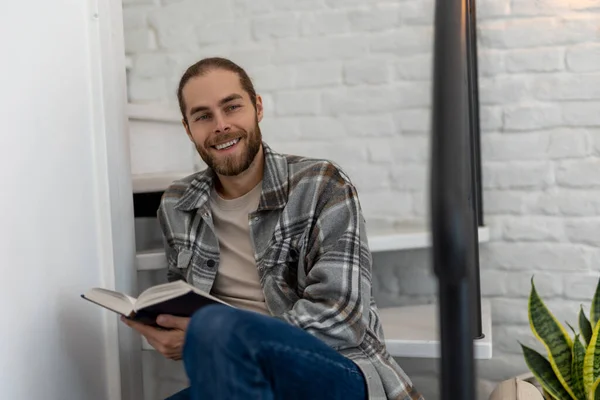 Radostný Mladý Muž Čtení Knihy Zatímco Sedí Schodech Svém Bytě — Stock fotografie