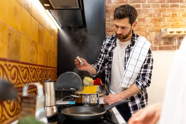 一个留着胡子的年轻人在厨房里做着健康的饭菜 在意大利面中加入盐 — 图库照片