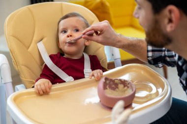 Küçük bebek babasıyla yemek yiyor, tanınmayan bir baba yeni yürümeye başlayan çocuğu besliyor..