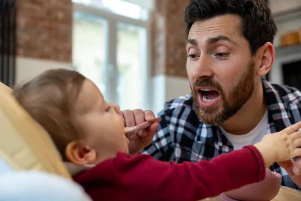 수염난 아버지 집에서 아기에게 먹이는 집안에서는 어린아이가 스푼으로 음식을 — 스톡 사진
