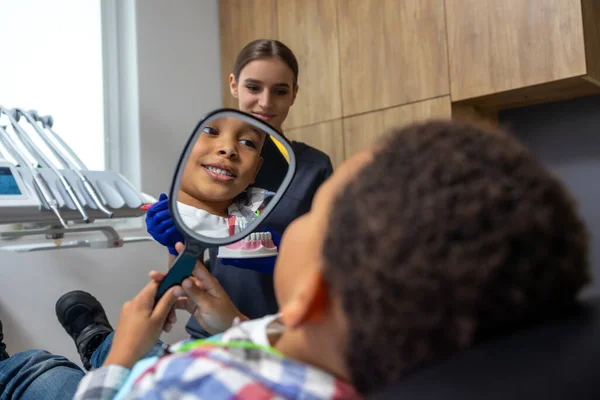 Dentistry Dark Skinned Boy Looking Mirror While Female Doctor Showing — Stock Photo, Image