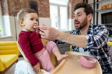 İlk yemeği yemleyin. Baba, bebeğini kaşıkla besliyor. Modern ev içinde öğle yemeği için..