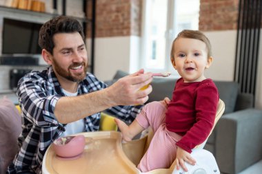 İlk yemeği yemleyin. Baba, bebeğini kaşıkla besliyor. Modern ev içinde öğle yemeği için..