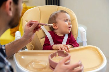 Tanımlanamayan baba, kucağında kaşıkla püre yiyen bebek ağlayan bebeği besliyor..