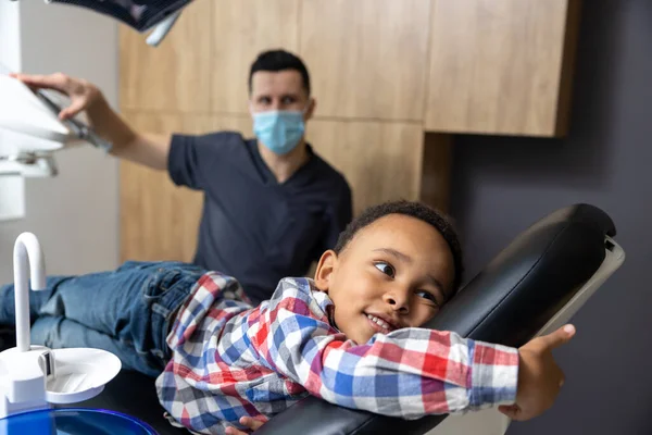 歯科医で 歯医者のオフィスで椅子に寝そべっている暗い肌の子供 — ストック写真
