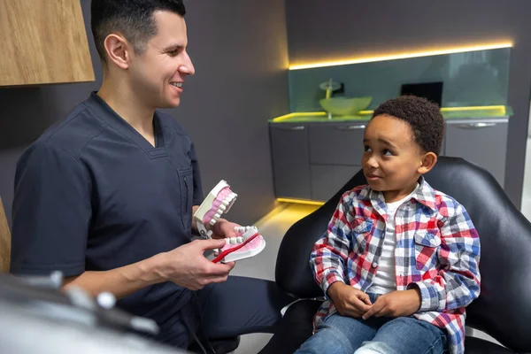 歯科医で かわいい男の子は彼に入れ歯を見せている医者の話を聞いて — ストック写真