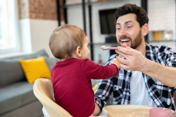 수염을 아버지는 현대식 실내에서 숟가락으로 귀여운 아기에게 먹이고 — 스톡 사진