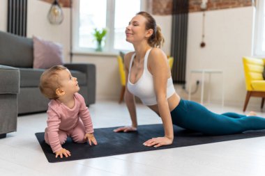 Sağlıklı gelişme. Atletik anne ve bebek evde birlikte egzersiz yapıp oturma odasında oynuyorlar..